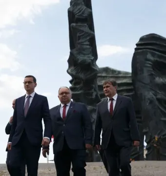 The Silesian Insurgents\' Monument rises behind a group of men in dark suits, with Polish flags near its base.