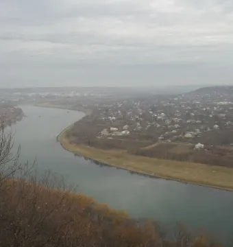Panoramic view of the Dnister River with buildings along both banks and bare tree branches in the foreground.