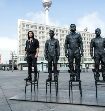 Anything To Say? sculpture with three dark statues and one person standing on chairs in a city plaza