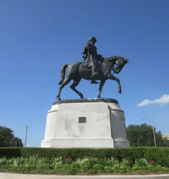 Gen. Beauregard equestrian statue on a tall stone pedestal, surrounded by hedges and flowers.