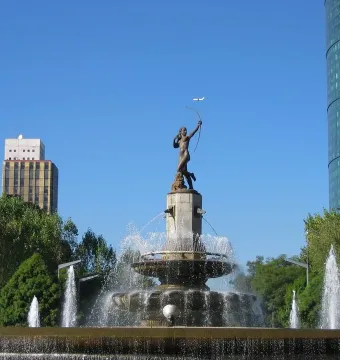 Diana the Huntress Fountain with a figure drawing a bow against a clear sky and city skyscrapers.