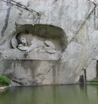 The Lion Monument shows a dying lion carved into a rock grotto, pierced by a spear, with inscriptions above and below and water in front.