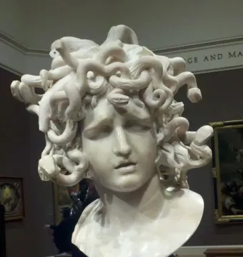 Bernini\'s Medusa marble bust with snake-like hair and a sorrowful expression in a museum gallery.