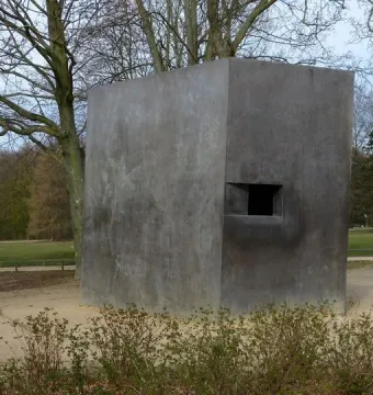 Memorial to Homosexuals Persecuted Under Nazism, a dark gray concrete block with a recessed opening in a park setting.