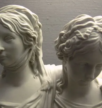 Close-up of the Princesses Monument showing two young women in a white sculpture, one facing forward and the other leaning in with her head lowered.