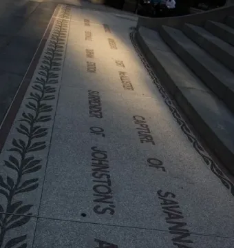 Granite paving with an engraved historical inscription beside the Sherman Monument, with a leaf pattern border and stone steps at right.