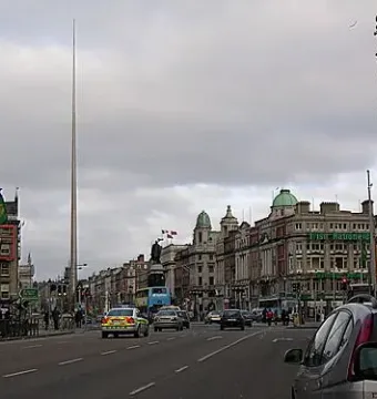 The Spire rises above Dublin street buildings under an overcast sky.