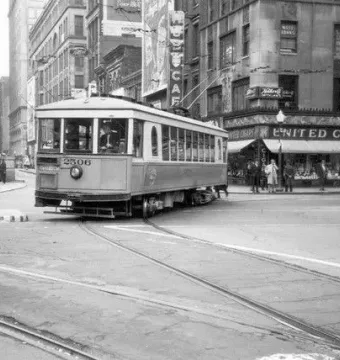 A streetcar passes a city intersection with the Tyler Davidson Fountain visible in the background.