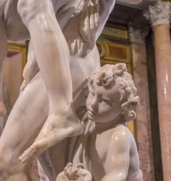 Marble sculpture detail of Ascanius beside the leg of Aeneas, holding a small vessel and looking upward.