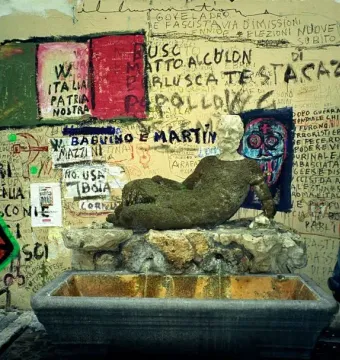 The Babuino Fountain, a weathered reclining stone statue with water flowing into a basin against a graffiti-covered wall.