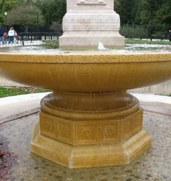 Butt–Millet Memorial Fountain with a shallow stone bowl, carved inscriptions, and an octagonal base in a pebbled basin.