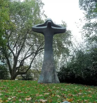 Der Mahner, a tall abstract bronze sculpture with upward-curving forms in a grassy park, with a plaque in front.