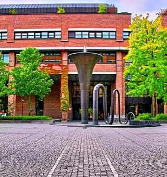 Erich-Schulze-Brunnen in a cobblestone plaza in front of a brick building with trees nearby.