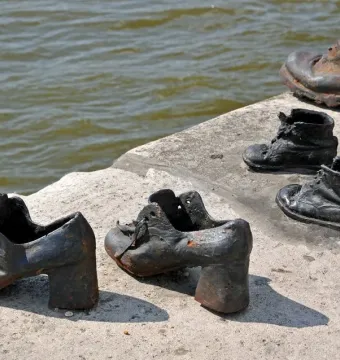 Metal shoes from the Shoes on the Danube Bank memorial on a concrete riverbank with calm water behind them.