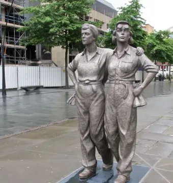 Women of Steel sculpture in Sheffield, showing two metal figures in work clothes on a dark base outdoors.