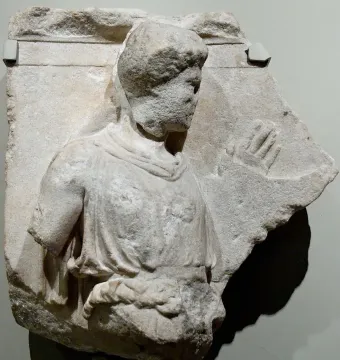 Damaged marble relief from the Bassae Frieze showing the upper body of a draped figure and a carved hand on the right.