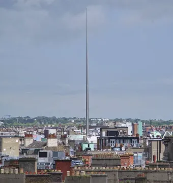 The Spire rises above Dublin rooftops and buildings under a cloudy sky.