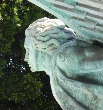 Close-up of the Monumento a Franco showing a verdigris-covered statue with wavy hair, draped clothing, and textured wings.