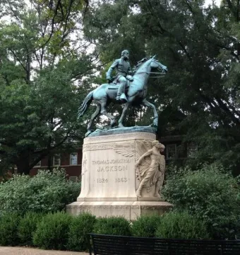 Stonewall Jackson equestrian statue on a stone pedestal surrounded by bushes and trees.