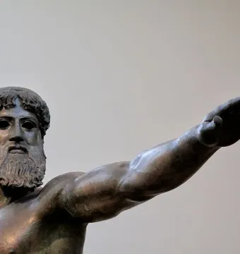 Artemision Bronze showing the upper torso and head of a bronze bearded man with curly hair and an extended arm.