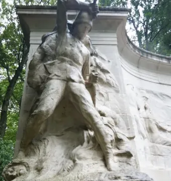 Stone relief from the Monument to the Belgian Pioneers in Congo showing a uniformed figure raising a tool above his head above French and Dutch inscriptions.