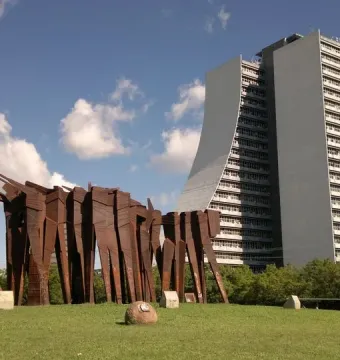 Monument to the Azoreans, a weathered steel abstract sculpture on a green lawn with a modern curved building behind it.