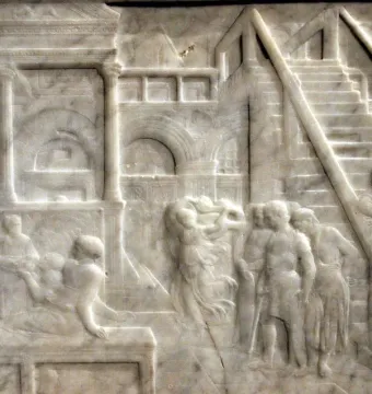 The Feast of Herod stone relief showing banquet figures beneath arches and stairs in a detailed architectural setting.