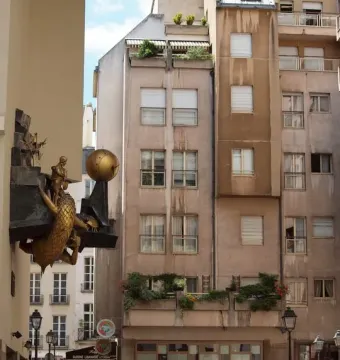 The Defender of Time sculpture shows a golden figure battling a scaly creature with a golden orb mounted on a building in Paris.