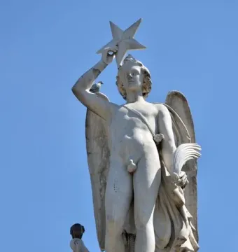 Weathered marble figure atop the Genio Catalán Fountain, holding a star overhead with pigeons perched on the base and shoulder.
