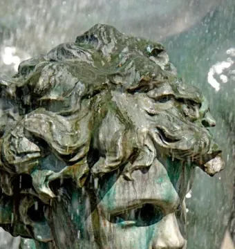Close-up of a weathered bronze head from the Monument aux Girondins, with curly hair and water flowing over the face.
