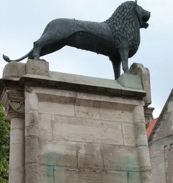 The Brunswick Lion statue on a stone pedestal, with two people holding white and black T-shirts below it.