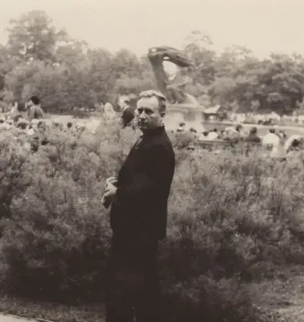 The Chopin Monument stands in a park with a crowd gathered around it and a man in a suit in the foreground.