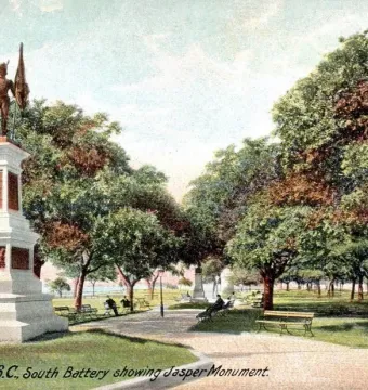 The Defenders of Fort Moultrie monument on a park path with benches and trees in Charleston.