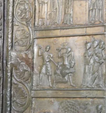Close-up of the Gniezno Doors showing a bronze relief panel with figures and decorative swirling borders.