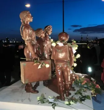 Kindertransport bronze sculpture of several children with suitcases on a plinth, decorated with flowers.