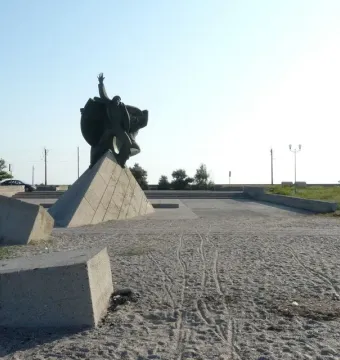 Monument of Eupatoria Assault showing three bronze figures on a large triangular concrete pedestal in a paved square.