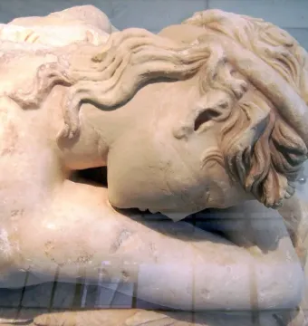 Close-up of the head and upper torso of the Sleeping Maenad marble sculpture, with wavy hair and a tilted resting pose.