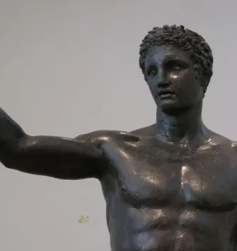 The Antikythera Ephebe bronze statue shown from the chest up, with curly hair and one arm raised.