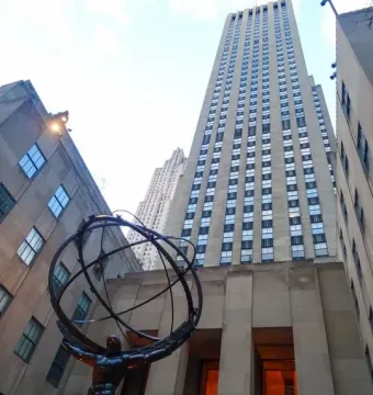 Atlas sculpture showing a kneeling muscular man holding up an armillary sphere in front of skyscrapers.