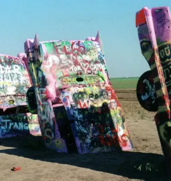 Cadillac Ranch with several vintage Cadillacs buried nose-down in a dusty field and covered in colorful graffiti.