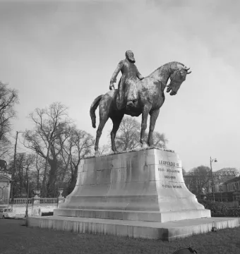 Leopold II equestrian statue on a tall stone pedestal in an open square with bare trees and surrounding buildings.