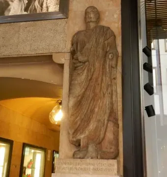 Scior Carera stone relief of a draped male figure set into a column beside a glass storefront.