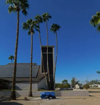 Veiled Homeless Jesus sculpture covered by a blue tarp on a white stand along a paved path.