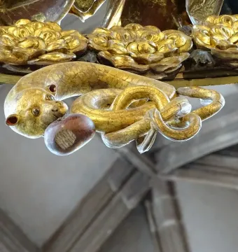 Close-up of the gilded serpent detail on the Angelic Salutation, holding a nut-like object in its mouth.