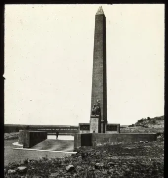 National Women\'s Monument with a tall obelisk and bronze figures at its base, seen from the steps below.