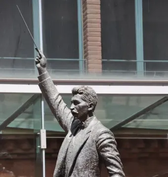 A bronze statue of Lluís Millet with a mustache, wearing a suit and bow tie and raising a conductor\'s baton.