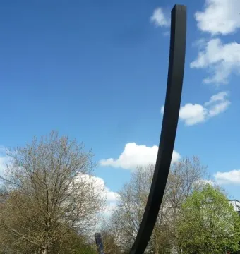 The Arc de 124,5° sculpture rises against a blue sky with clouds in Berlin.