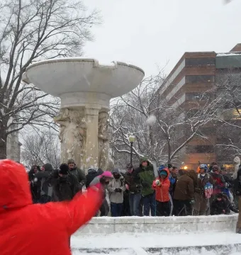 Dupont Circle Fountain partially covered in snow with people gathered around it in a winter park.