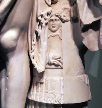 Detail of the General of Tivoli showing a carved face and draped fabric on the marble support beside a muscular leg.