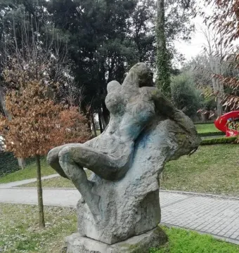 Güzel İstanbul stone sculpture leaning back against a rocky outcrop along a paved path with trees nearby.